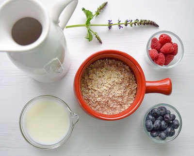 Oats in a bowl, a cup of milk and two bowls with staw berries and blue berries